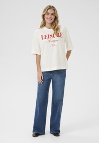 Light cream oversized t-shirt with red "LEISURE League" print, paired with blue wide-leg jeans. Smooth fabric, relaxed fit, simple design.