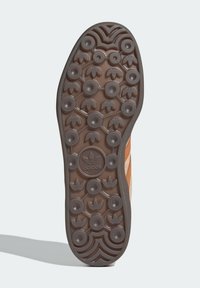 Brun gummisula på sneakers med cirkulärt mönstrat grepp, med Adidas-logotyp i mitten. Ovandel i ljusbrunt mocka med framträdande randiga detaljer.