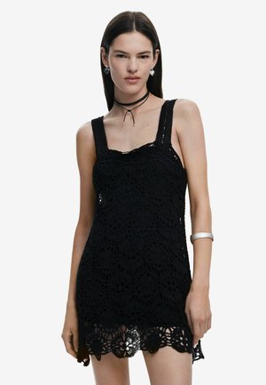 Schwarzes Spitzenkleid mit floralem Häkelmuster, quadratischem Ausschnitt und breiten Trägern. Verfügt über einen gewellten Saum und eine durchsichtige Textur, kombiniert mit minimalem Zubehör.