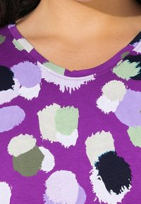 Fialová košile s krátkým rukávem, zdobená velkými abstraktními puntíky v zelené, levandulové, černé a bílé barvě, s kulatým výstřihem a hladkou texturou.