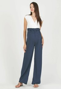 Combinaison bleu marine avec des pois blancs, une taille froncée ajustée et un col en v style cache-cœur. Fabriquée en tissu doux et léger avec des jambes larges.