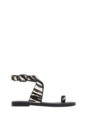 Płaska sandałka z czarno-białymi paskami w zebra print, klamrą przy kostce i pętlą na palec na czarnej podeszwie.