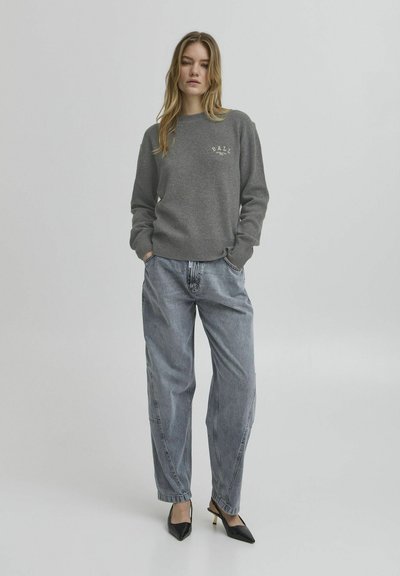 Grauer gestrickter Pullover mit geripptem Saum und kleinem "BALI"-Logo, kombiniert mit lockeren hellblauen Jeans und schwarzen spitzen Pumps.
