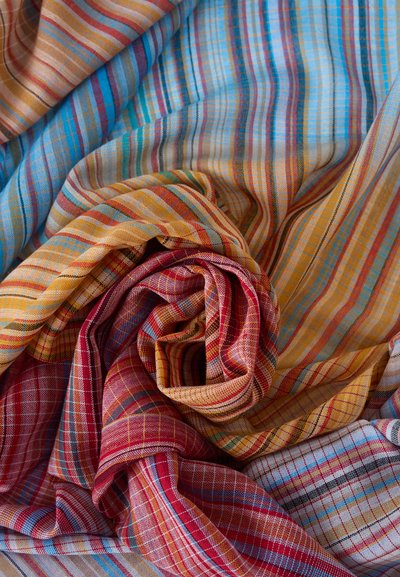 Χρωματιστό καρό ύφασμα με σχέδια σε κόκκινο, κίτρινο, μπλε και πορτοκαλί, χαλαρά διπλωμένο και στρωμένο για να δημιουργήσει υφή και βάθος.