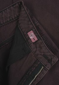 Zbliżenie na pas ciemnofioletowych spodni z regulowanym guzikiem i częściowo otwartym suwakiem.