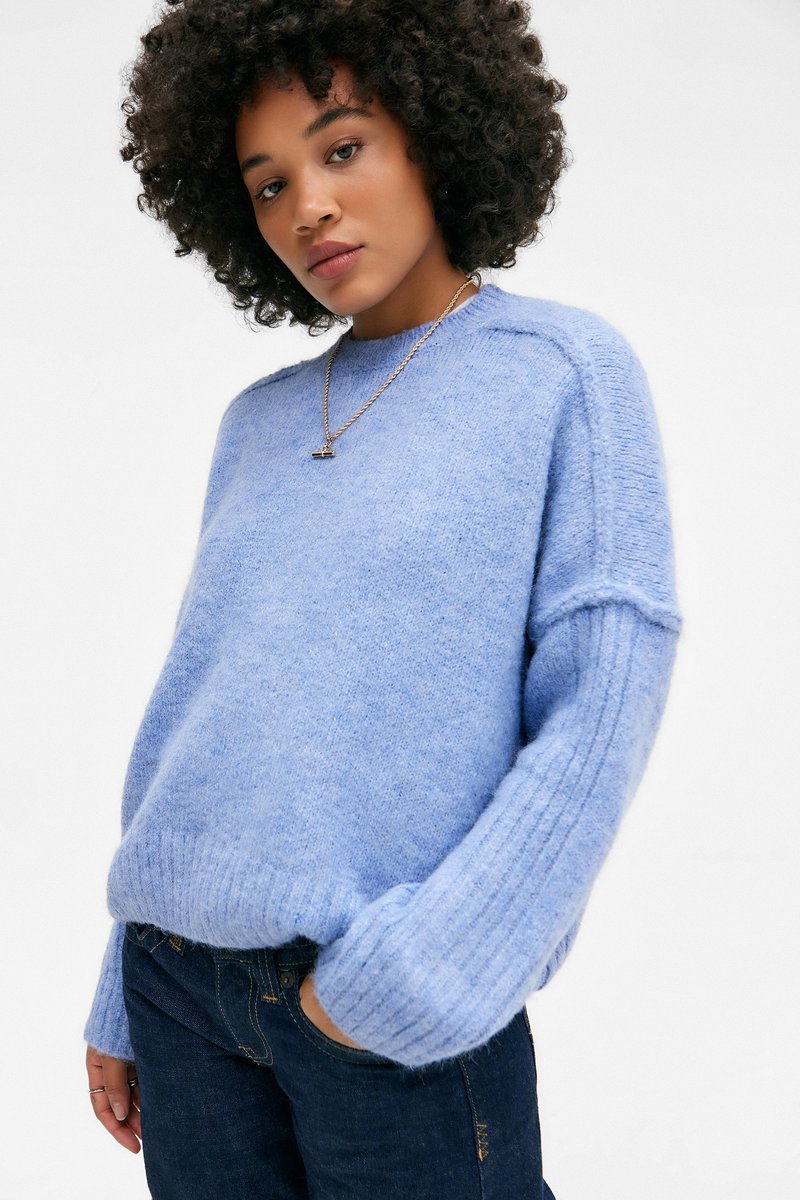 Lys blå strikkegenser med en myk tekstur, ribbestrikkede mansjetter og avslappet passform, kombinert med mørke denimjeans. Minimalistisk design uten mønstre.