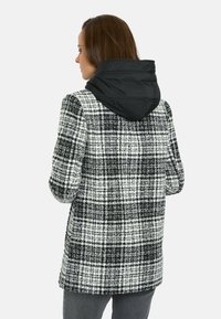 Abrigo de cuadros con colores blanco y negro, un exterior texturizado y una capucha acolchada negra para mayor calidez y estilo.