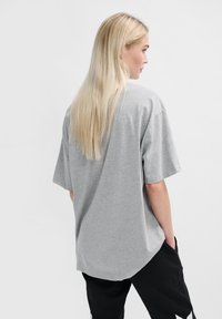 Grå oversized t-shirt med korta ärmar, rundad nederkant och avslappnad passform, tillverkad av ett mjukt material. Modellen står med ryggen mot kameran.