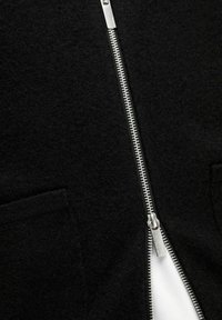 Svart jacka med dragkedja i en mjuk, texturerad kvalitet. Har en silverfärgad dragkedja fram och två sidofickor. Vit inre foder.