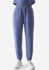 Pantalones jogger de color azul claro con cintura elástica y tobillos ajustados, fabricados con una tela suave y elástica. Combinados con zapatillas blancas.