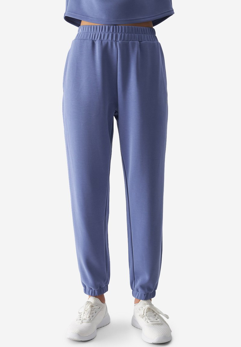 Pantalones jogger de color azul claro con cintura elástica y tobillos ajustados, fabricados con una tela suave y elástica. Combinados con zapatillas blancas.