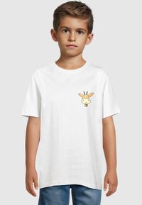 Hvid bomulds t-shirt med et cartoon giraffemotiv på venstre bryst. Korte ærmer og rund halsudskæring. Bæres med blå denim shorts.