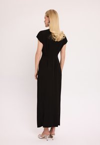 Czarna długa sukienka z krótkimi rękawami w formie peleryny, dopasowanym gorsetem i zwiewnym krojem. Tkanina wydaje się gładka i miękka, z rozcięciem z tyłu.