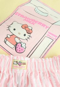 Tela de rayas rosas y blancas con un parche que muestra a Hello Kitty sosteniendo una fresa y un cartón rosa etiquetado "Leche de fresa."