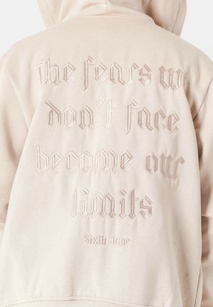Beige Hoodie mit gesticktem Text auf dem Rücken: "Die Ängste, denen wir uns nicht stellen, werden zu unseren Grenzen" mit dem Markennamen "Sixth June."