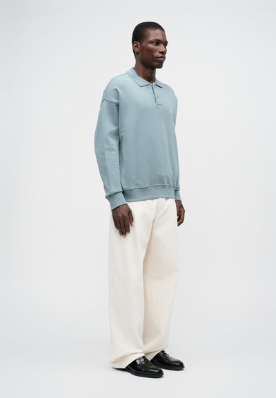 Ljusblå sweatshirt med krage, avslappnad passform och ribbade mudd, kombinerad med krämfärgade vida byxor och svarta loafers. Minimalistisk design.