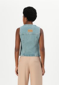 Lyseblå denimvest med baklapp, uten ermer og rå kant. Kombinert med beige stripete vide bukser.