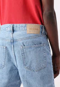 Jeans de denim azul claro con una cintura de altura media, que presentan una tela texturizada, dos bolsillos traseros y una etiqueta de cuero marrón etiquetada como "ONLY & SONS".