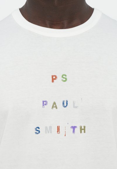 Fehér pamut póló, multiszínű, texturált betűzéssel, „PS PAUL SMITH” felirattal, különböző betűméretekben. Kerek nyakú dizájn.