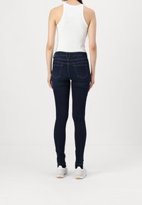 Dark blue skinny jeans with a high waist, made of denim, featuring back pockets and subtle stitching details. Paired with white sneakers.