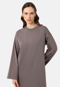 Robe grise à manches longues en tissu doux, avec un col rond et une coupe ample ; dotée de coutures minimalistes et de manches larges.
