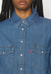 Helles blaues Denim-Hemd mit Button-Down-Kragen, zwei Brusttaschen und silbernen Knöpfen. Verfügt über das rote Levi's-Logo auf der linken Tasche.