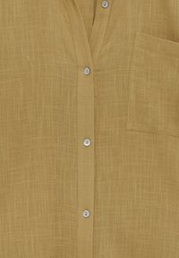 Chemise jaune moutarde en tissu léger, avec une finition texturée, une poche à l'avant et une fermeture boutonnée avec des boutons argentés.