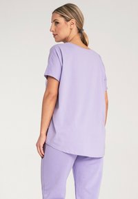 Liliowa koszulka z krótkim rękawem i okrągłym dekoltem, w połączeniu z dopasowanymi liliowymi spodniami. Gładki materiał o luźnym kroju, minimalne przeszycia.