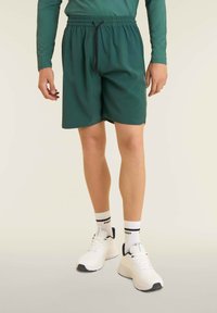 Pantalones cortos verdes con cinturilla elástica, cierre de cordón y una textura suave. Combinados con zapatillas blancas y calcetines de estampados.