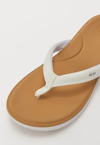 White synthetic flip-flop with a tan footbed and white accents. Contoured sole, thin straps, and a toe post for secure fit.