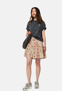 T-shirt oversize gris foncé, jupe à motifs floraux avec des accents rouges et bleus, sac à épaule gris et baskets métalliques.