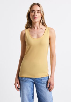Top giallo senza maniche con scollo rotondo, realizzato in tessuto liscio; abbinato a jeans a gamba larga blu. Nessun motivo o dettaglio metallico.