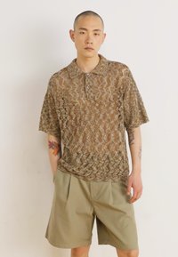 Brown and beige patterned short-sleeve polo shirt with a collar, featuring a textured knit design. Paired with light green pleated shorts.