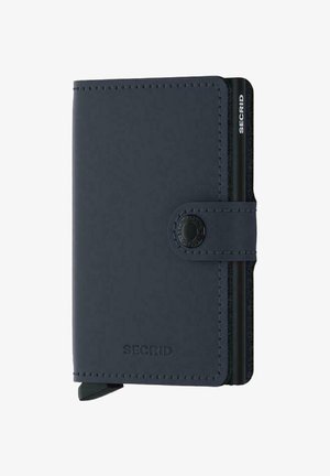 Portefeuille en cuir bleu marine avec fermeture à bouton-pression, présentant un design épuré, des coutures discrètes et des emplacements pour cartes sur le côté. Marque visible.