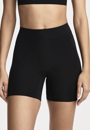 Woman wearing high-waist black athletic shorts and a matching black sports bra, standing with arms relaxed by her sides.