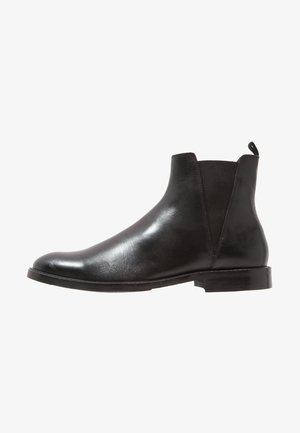 Stivaletto Chelsea nero in pelle con pannelli laterali elastici e tacco basso impilato, mostrato di profilo su sfondo bianco.