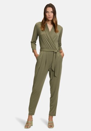 Tuta verde oliva con design avvolgente, maniche lunghe e cintura in vita. Presenta tasche laterali e aperture delle gambe affusolate.