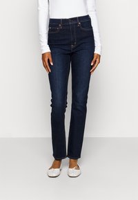 Jeans de mezclilla azul oscuro con un diseño de cintura alta y pierna recta, y costuras en contraste. Estilo de cinco bolsillos con cierre de botón.