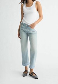 Top bianco a righe con logo, jeans azzurri con orlo in pizzo floreale e ballerine nere decorate. Design semplice con vestibilità rilassata.