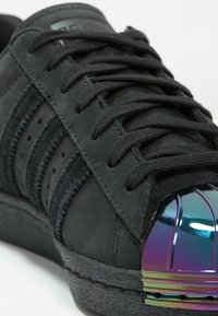 Sneaker in suede nero con tomaia testurizzata, tre strisce orizzontali e punta lucida iridescente. Presenta lacci neri e suola in gomma.