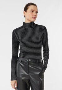 Czarny golf w paski z długimi rękawami, ozdobiony poziomymi metallicznymi paskami. Połączony z czarnymi, wysokim stanem, skórzanymi spodniami.