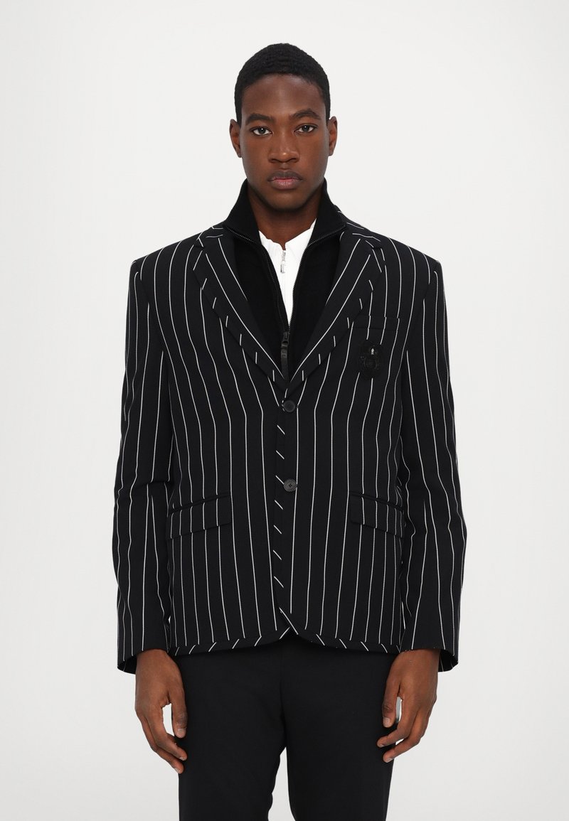 Black pinstripe blazer made of thick fabric, featuring a notched collar, front buttons, and two flap pockets. Textured black interior.