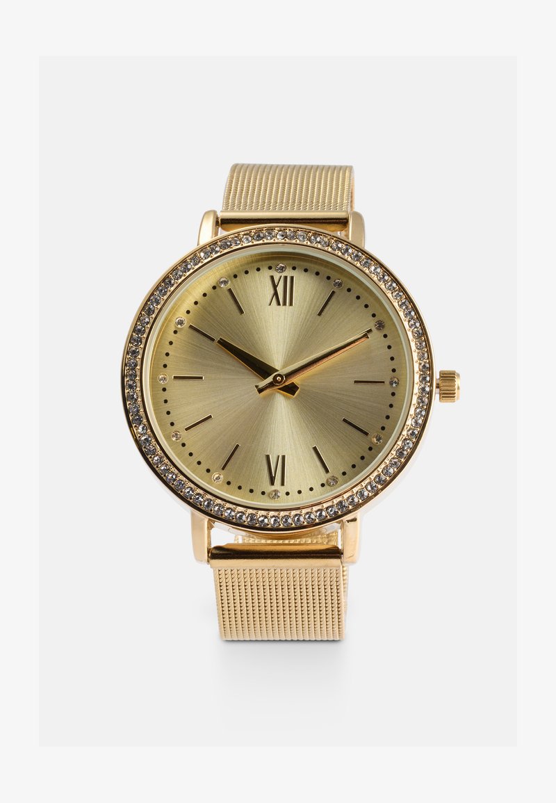 Orologio dorato con cassa rotonda, quadrante in oro testurizzato, indicatori delle ore e accenti di cristallo. Presenta un cinturino a rete e una corona sul lato.