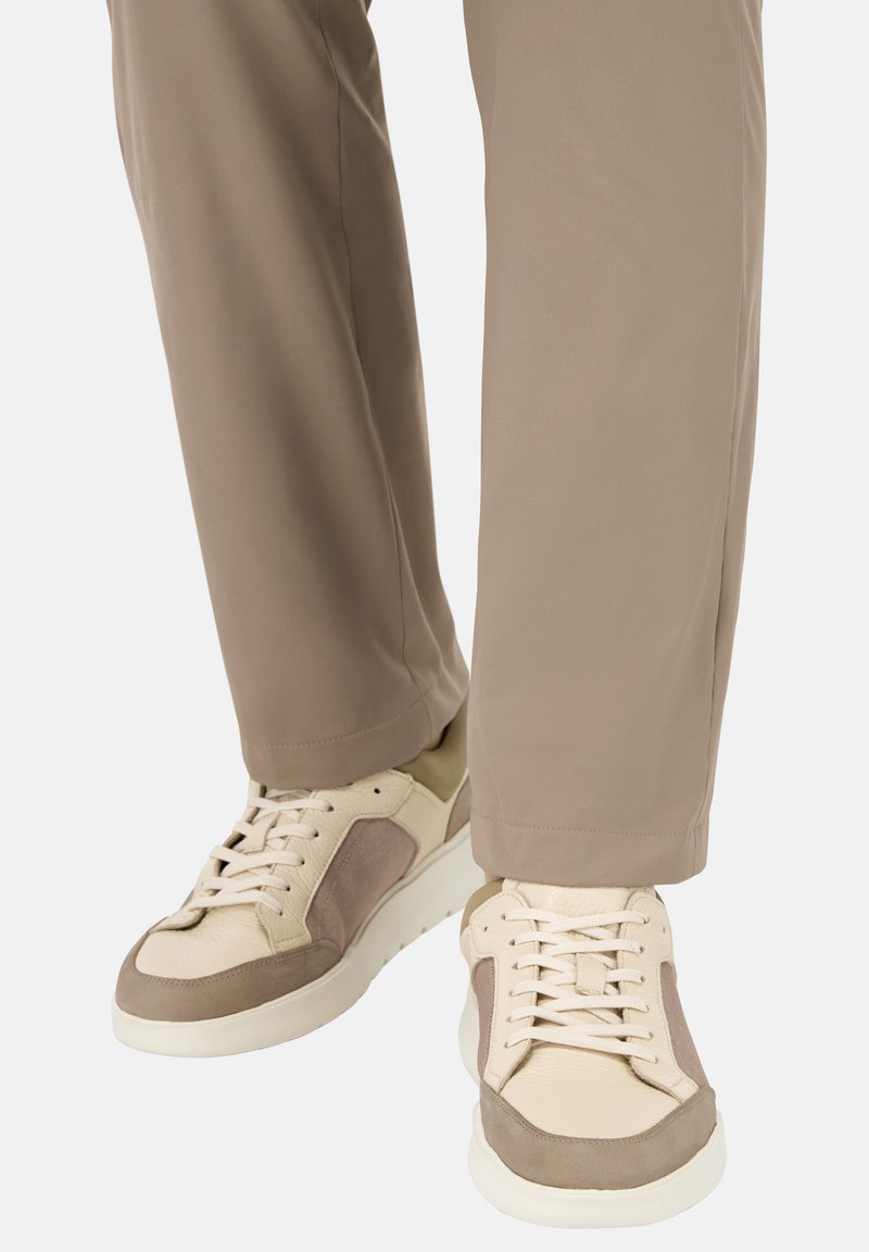 Beežid ja hallid jooksujalatsid, millel on tekstureeritud viimistlus, paelad, külgpanelid ja paks valge tald, kombineeritud heleda pruuni pükstega.