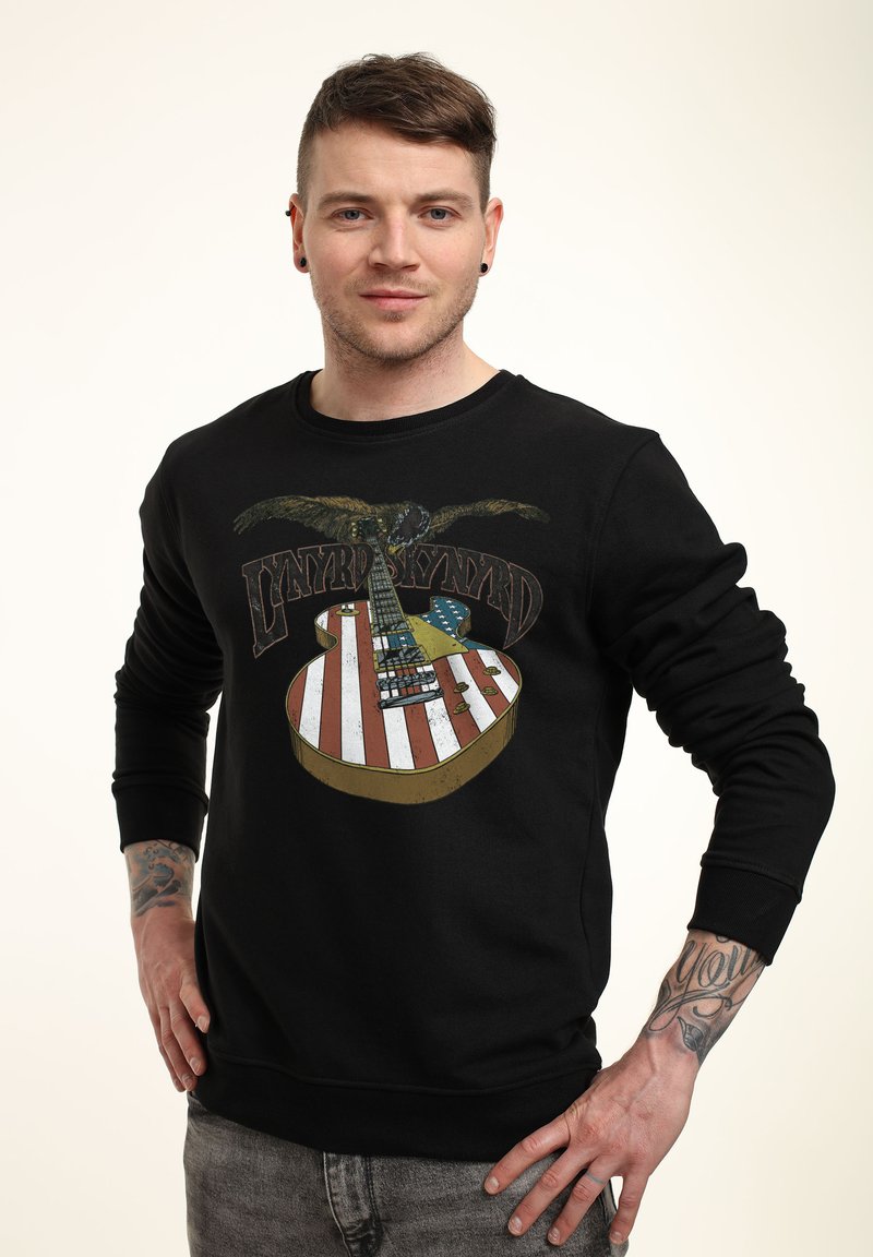 Sudadera negra con un diseño gráfico de una guitarra con rayas rojas y blancas, un águila y el texto "Lynyrd Skynyrd" en un estilo clásico.