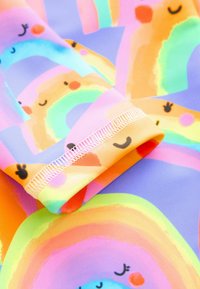 Tela multicolor con arcoíris sonrientes y patrones juguetones. Textura suave, tonos pastel de rosa, naranja y azul, con detalle de puño cosido.