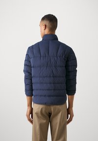 Marineblå puffjakke med høy krave og horisontal quiltedesign. Slim fit med cropped ermer, glatt tekstur og lett materiale.