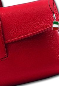 Sac en cuir rouge avec une surface texturée, doté d'un fermoir à rabat et d'un charm décoratif avec un design du drapeau italien.