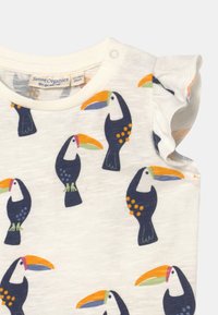 Camisa de manga curta em creme claro com estampado colorido de tucano. Apresenta fechos de pressão no ombro e bordas das mangas com babados. Feita de tecido macio.