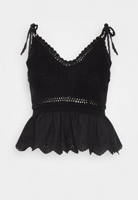 Top peplum negro de punto con tirantes ajustables, que presenta un dobladillo en forma de onda y detalles de ojales alrededor del borde inferior.